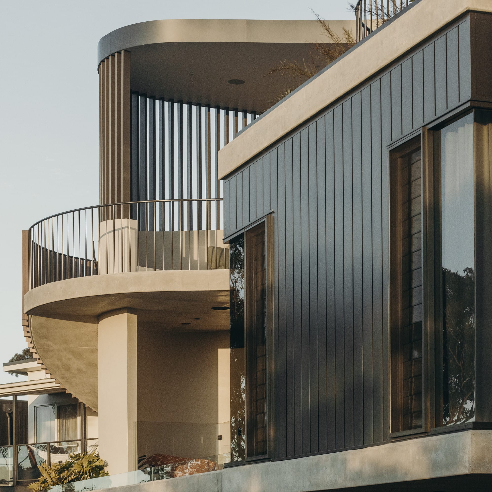 Premium residence clad in dark standing-seam aluminium panels with a curved batten-screened balcony