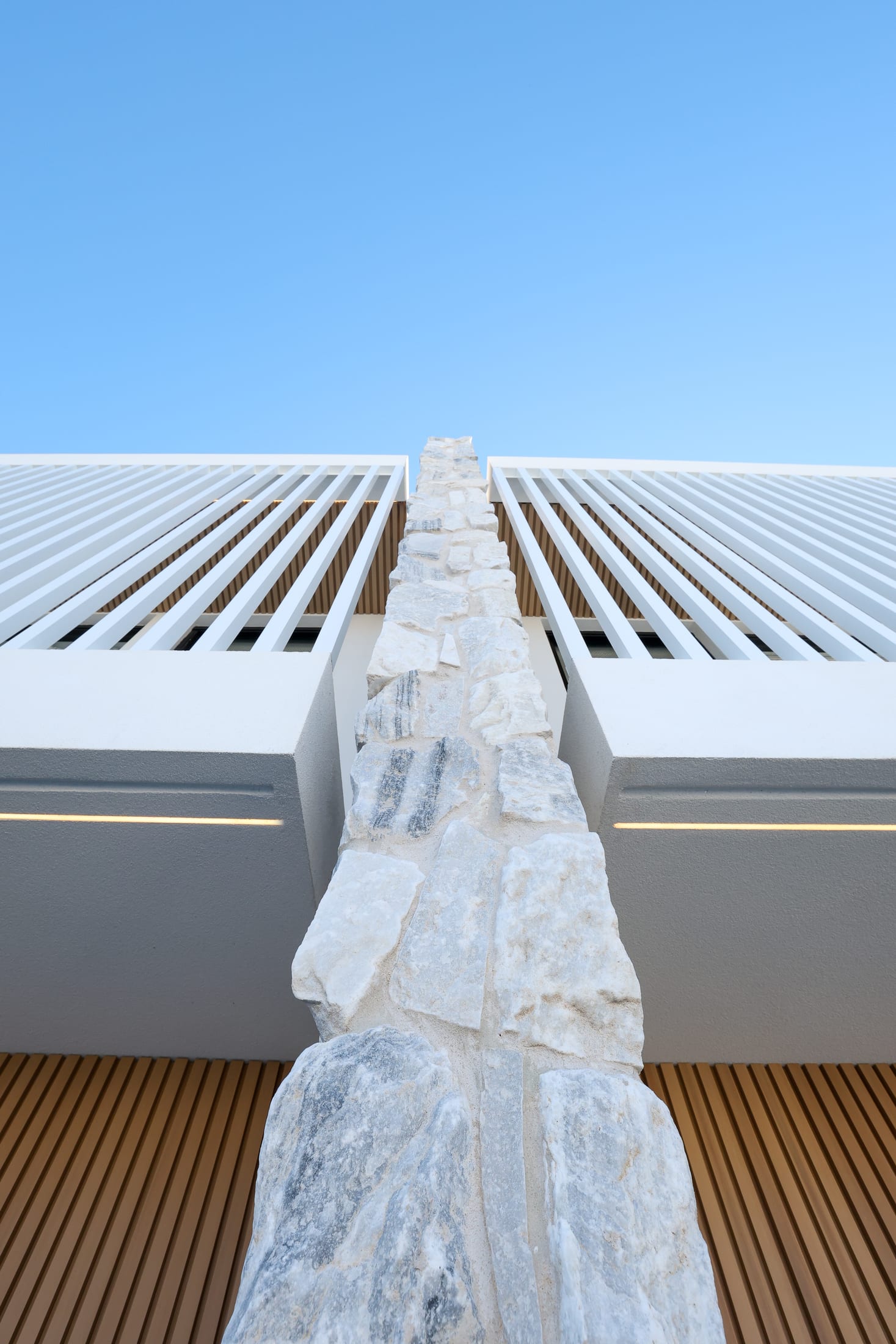 Abbotsford residence — white batten louvres flanking a natural stone spine under a clear blue sky